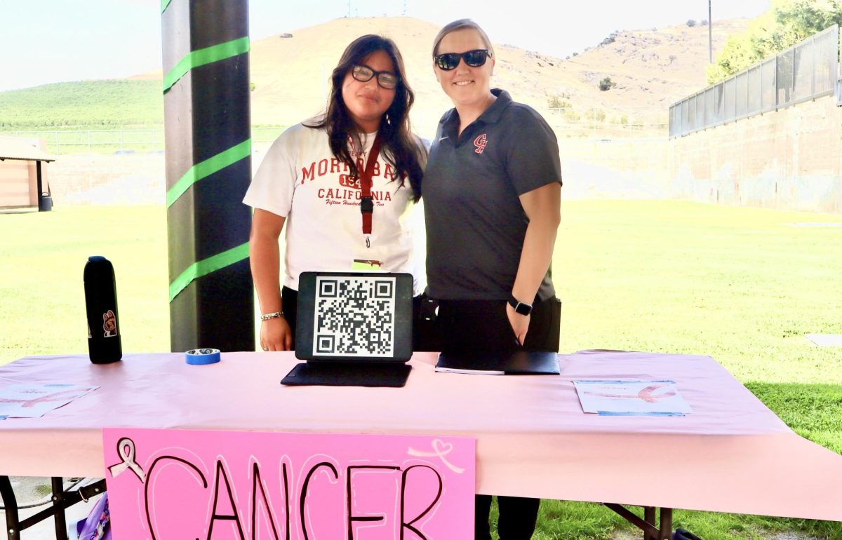 Jackie Gomez and Ms. Schieler stand in front of the Cancer Awareness Club booth during club rush week. 